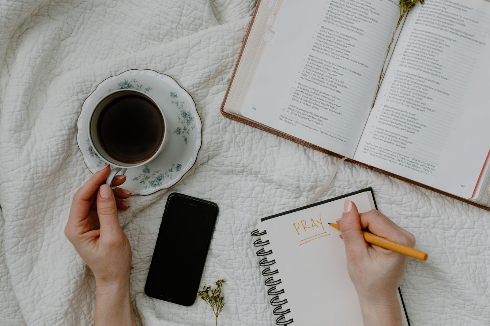 Hands writing in a notebook beside a cup of tea and an open book.